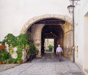 Persona mayor caminando bajo arcos en las calles de Spoleto, Italia, verano de 2019.