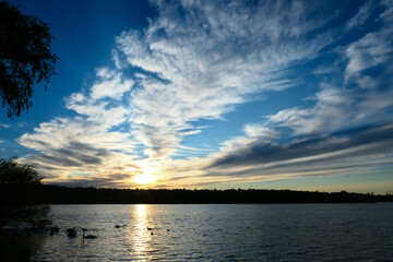 Amazing sunset over the water. Beautiful landscape with a lake and dramatic sky with cumulus clouds on the horizon.