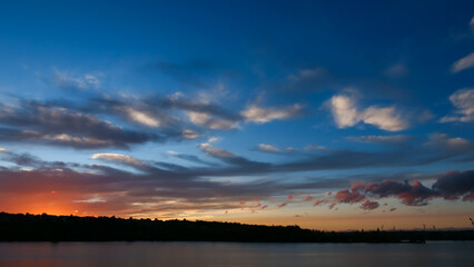 Amazing sunset over the water. Beautiful landscape with a lake and dramatic sky with cumulus clouds on the horizon.