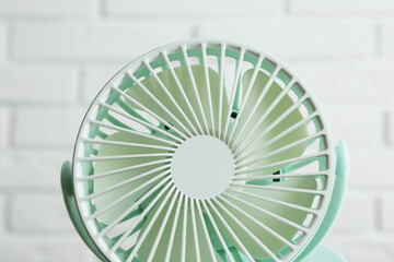Portable fan near white brick wall, closeup. Summer heat