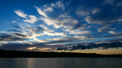 Amazing sunset over the water. Beautiful landscape with a lake and dramatic sky with cumulus clouds on the horizon.