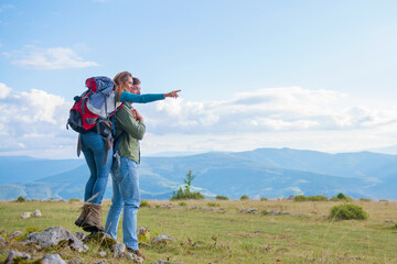 Two hikers with backpack standing on top of a mountain and look