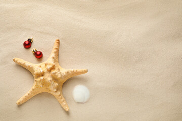 Fototapeta na wymiar Beautiful starfish, shell, festive balls and space for text on sand, flat lay. Christmas vacation