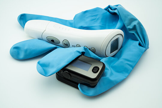 Fiberthermometer, Pulsoxymeter und ein blauer Gummihandschuh vor wei&szlig;em Hintergrund freigestellt.