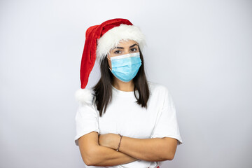 Fototapeta na wymiar Young beautiful woman wearing a christmas hat over white background wearing the coronavirus medical mask.