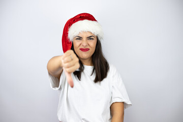 Young beautiful woman wearing a christmas hat over white background with angry face, negative sign showing dislike with thumb down