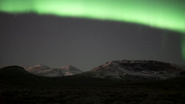 Bright aurora borealis and stars over snowy mountain peaks and tundra moss
