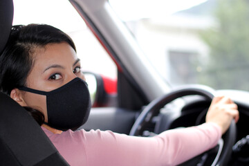 latin woman driver with protection mask in vehicle interior, new normal when driving