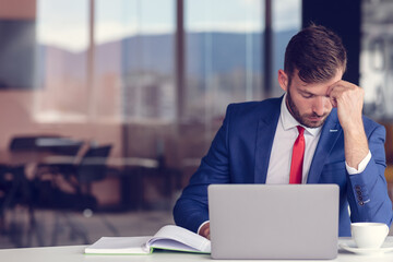 Feeling exhausted. Frustrated young beard man keeping eyes closed while sitting at his working place in office
