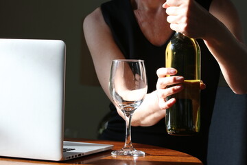 Mature woman at home office desk with a bottle of white wine with laptop and covid face mask sitting on desk 
