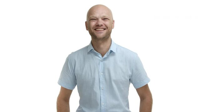 Video of cheerful bald guy with beard, smiling and laughing at something funny, standing happy over white background in casual blue shirt