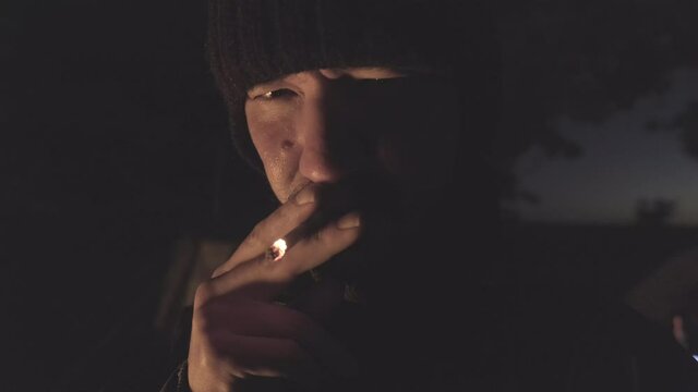 Man smokes cigarette in front of the camera at night