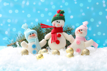 Cute toy snowmen, fir branch and Christmas balls on snow against blurred background