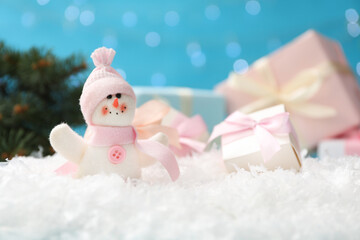 Cute toy snowman and gift box on snow against blurred background