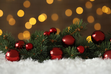 Fototapeta na wymiar Fir branches with Christmas balls on snow against blurred festive lights