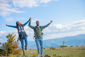 Happy travelers couple conquered top of mountain, raises hands up