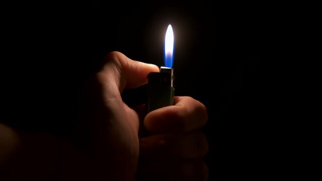 The lighter in the man's hand lights up and burns. Sparks
