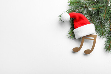 Decorative music note with Santa hat near fir tree branch and space for text on white wooden...