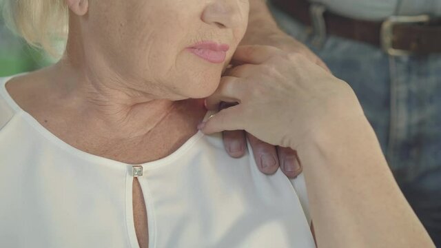 Close-up of unrecognizable old woman taking hand of senior man. Couple of Caucasian retirees in sunny summer park outdoors. Concept of support and love.
