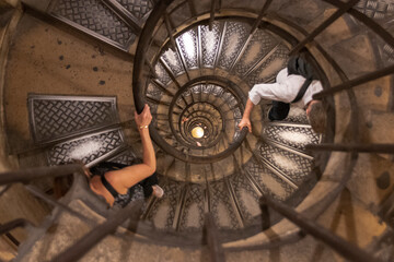 A tourist looks down the center of a spiral staircase as other tourists climb up at the Arc de Triomphe in Paris, France.