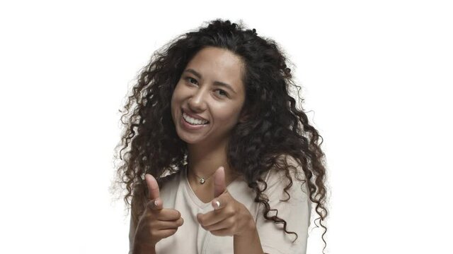 Close-up of attractive cheeky woman with dark curly hair, pointing fingers at camera and smiling, need you, standing in casual t-shirt over white background