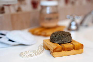 Modern and ecological wooden soap holder on a bathroom counter, with soap and shampoo in a bottle along with a reusable cleaning pad. for body care