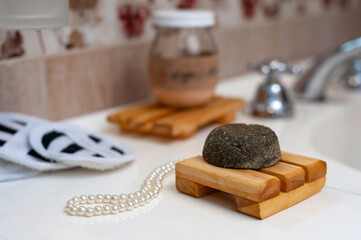 Modern and ecological wooden soap holder on a bathroom counter, with soap and shampoo in a bottle along with a reusable cleaning pad. for body care