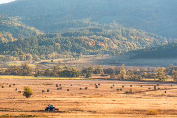 Fototapeta premium Lonely tractor harvest hay field crop stubble golden yellow orange autumn mountain background massive bulgaria technology machine agriculture