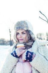 young pretty teenage hipster girl outdoor in winter snow park having fun drinking coffee, warming up happy smiling, lifestyle people concept