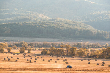 Fototapeta premium Lonely tractor harvest hay field crop stubble golden yellow orange autumn mountain background massive bulgaria technology machine agriculture