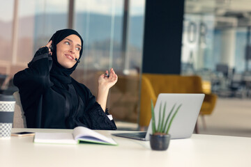 Happy muslim businesswoman in hijab at office workplace. Smiling Arabic woman working on laptop and...