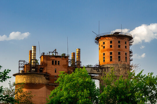 an abandoned brick industrial structure with lightning rods and rusty chimneys against a blue sky with cumulus clouds
