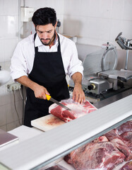 Friendly butcher is cutting meat for clients in market