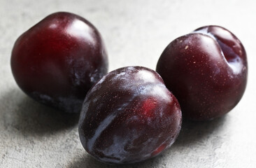 Three ripe plums on a background of a gray table top in the kitchen. A portion of fruits.