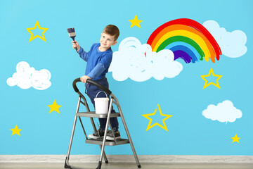Cute little boy painting rainbow and clouds on wall