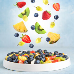 Plate with delicious fruit salad and flying ingredients on color background