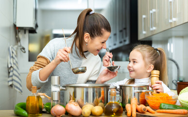 Happy young mother and small daughter tasting vegetable soup together