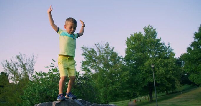Cute little boy jumping from the rock in the summer park. Red cinema camera. Slow motion 4k