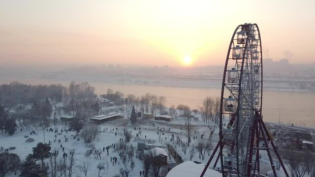 Irkutsk Ferris Wheel and city in winter snow, people iceskating, aerial sunset
