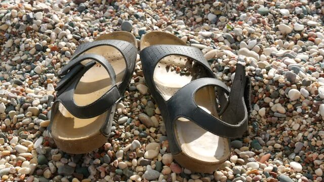 Lonely leather sandals on the beach of rocky pebble sand on the seashore in summer, vacation concept.