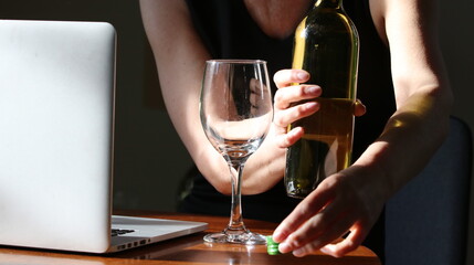 Mature woman at home office desk with a bottle of white wine with laptop and covid face mask sitting on desk 