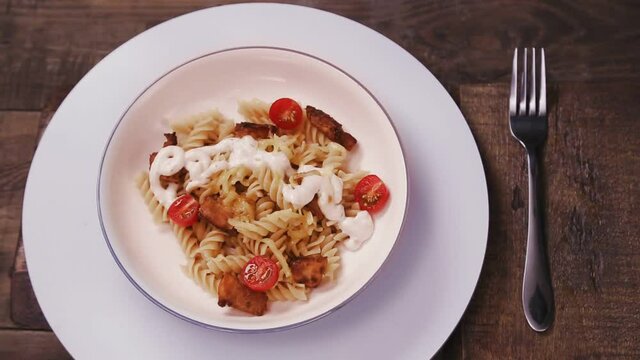 Pasta with chicken and cheese with tomato on a gray plate rotates in a circle next to a fork