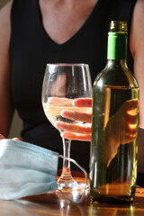 Mature woman at home office desk with a bottle of white wine with laptop and covid face mask sitting on desk 