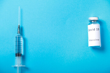 On a blue background, a syringe and a vial of coronavirus vaccine.