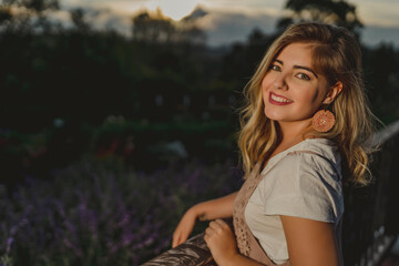 Beautiful blonde woman smiling on a balcony with a sunset on the background