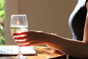 Mature woman in home office with laptop and grubby wine glass of white wine