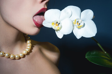 Sexy girl lick orchid flower. Orchids oral tongue. Sensual young woman suck floral orchidea.