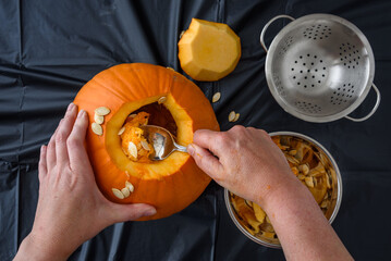 Pumpkin seed harvesting, woman’s hand scooping seeds out of fresh pumpkin with a spoon
