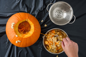 Pumpkin seed harvesting, woman’s hand scooping seeds out of fresh pumpkin with a spoon

