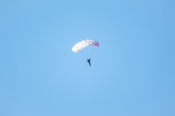one parachutist floats slowly at low altitude on the background of clear sky